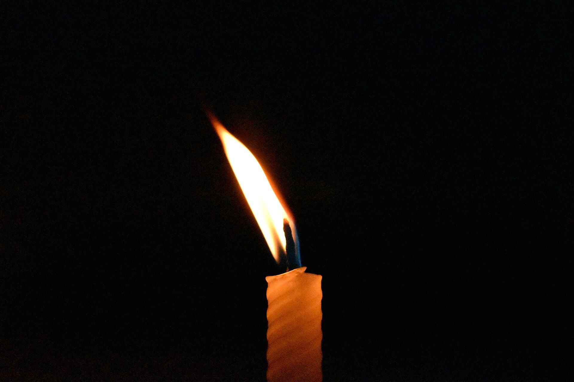 A single lit candle glowing in the darkness, symbolizing remembrance