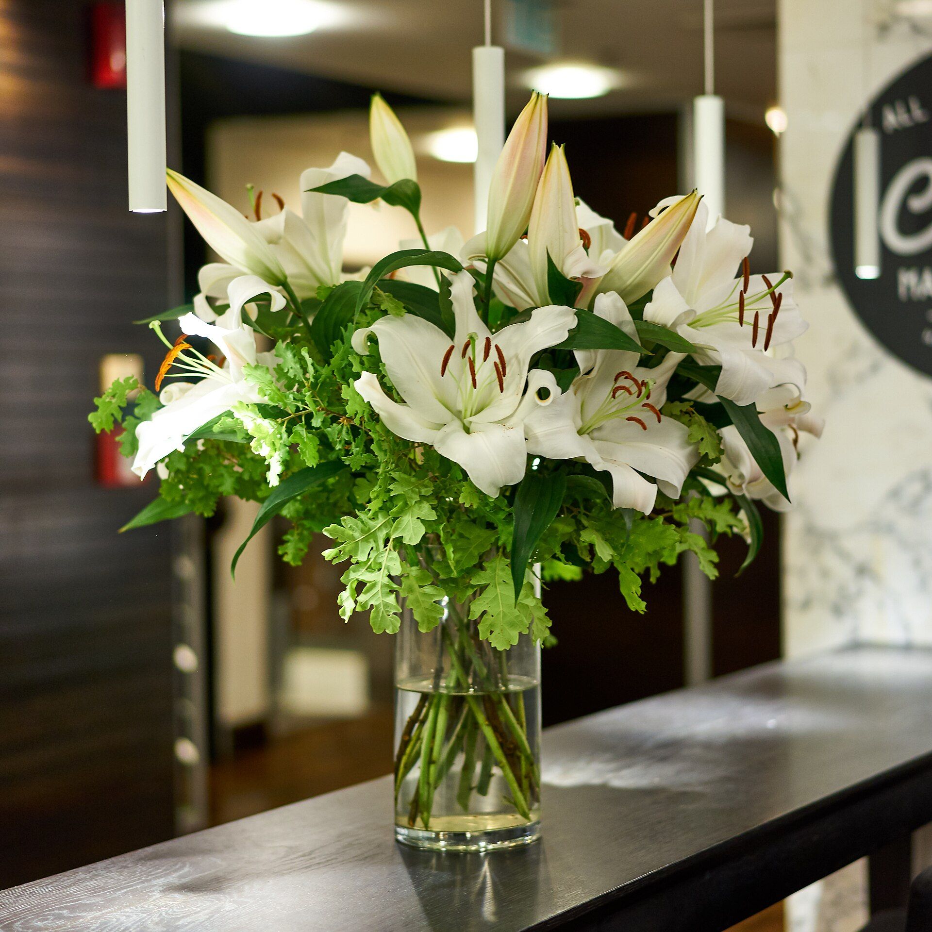 An elegant arrangement of white lilies displayed in a calm, softly lit reception space